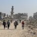 Refugees walk down a road in Gaza, surrounded by ruined buildings.